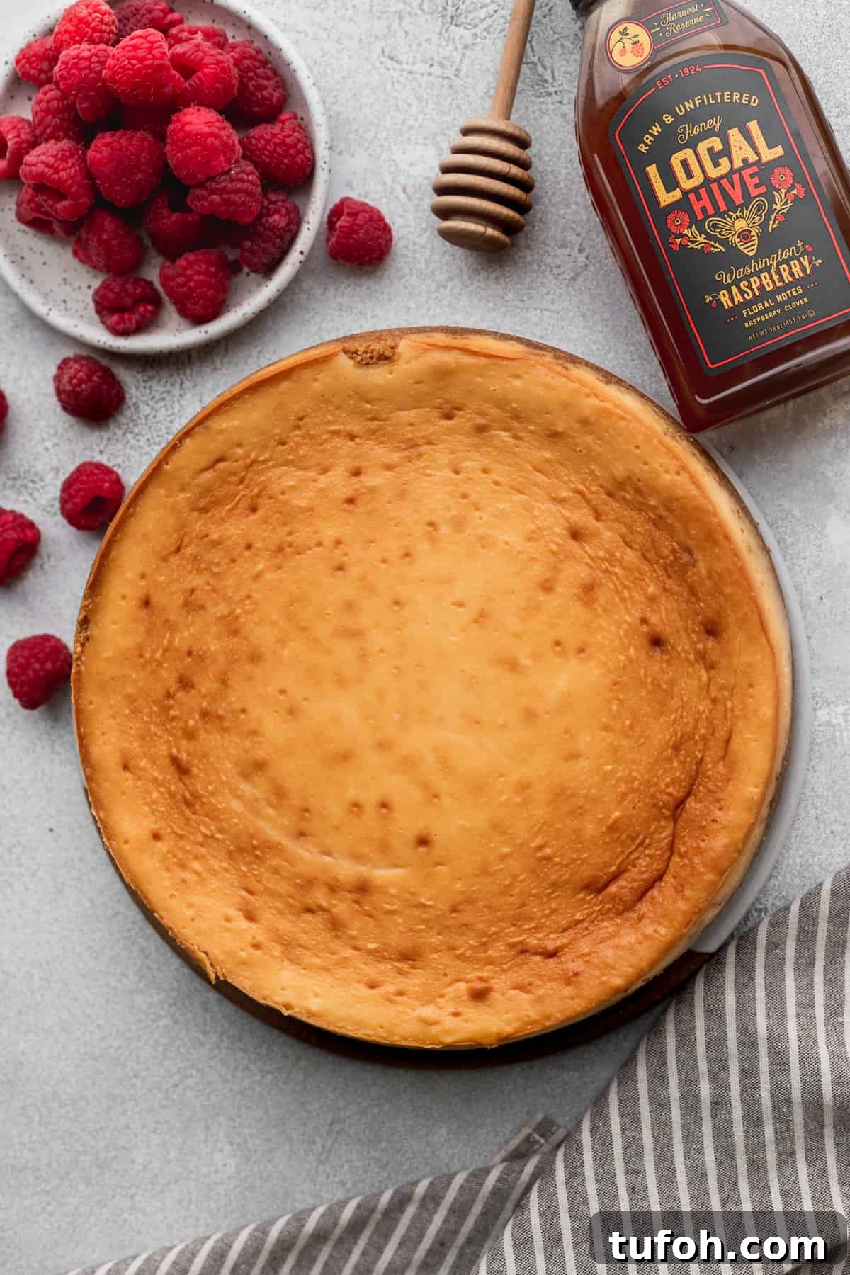 Decadent Honey Cheesecake Recipe with Silky Cream Filling 9 Baked cheesecake on a platter surrounded by raspberries.
