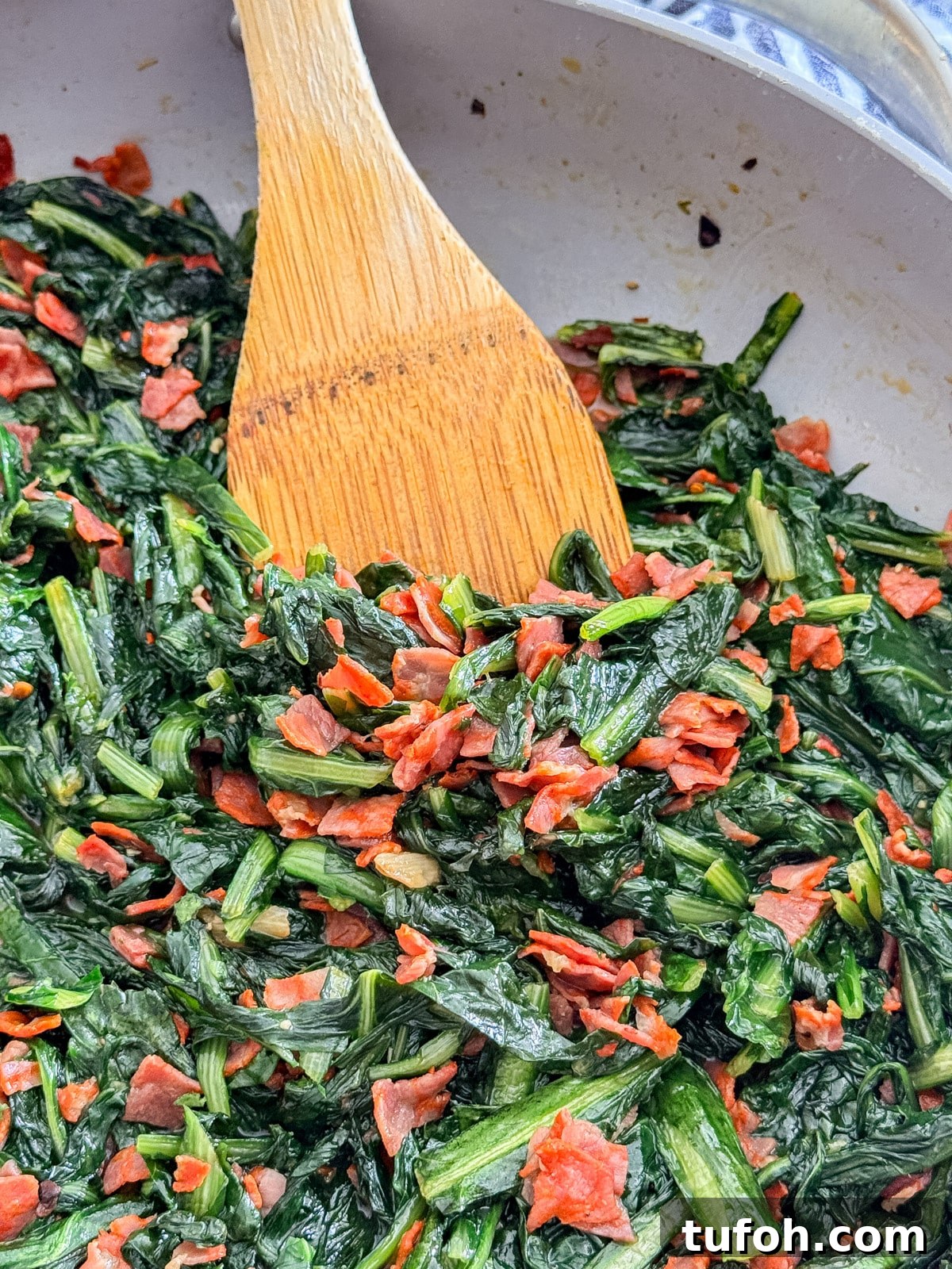 A close up of a pan of dandelion greens with a wooden spoon in it.