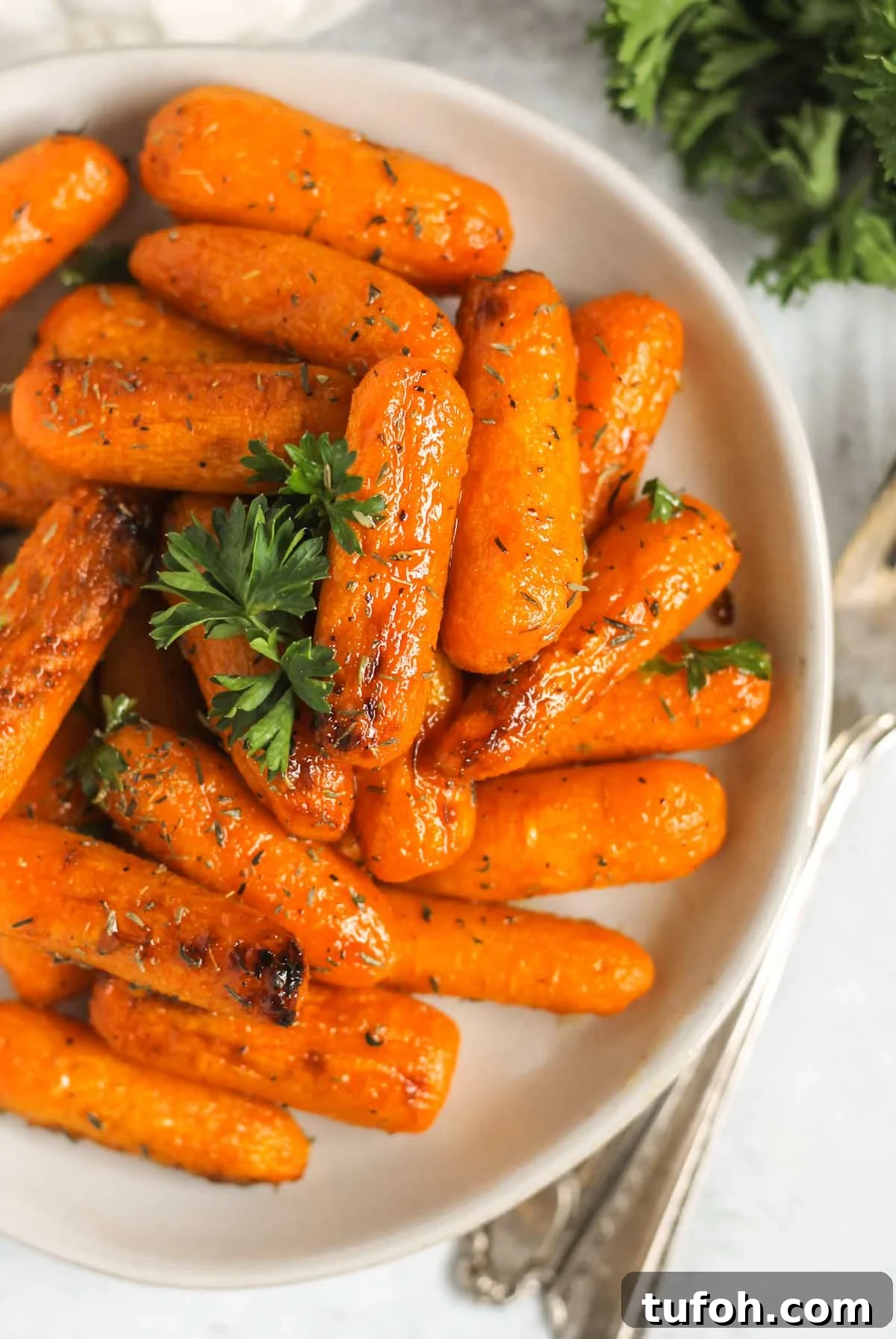 Roasted baby carrots sprinkled parsley on a small plate with vintage forks laying next to the plate.