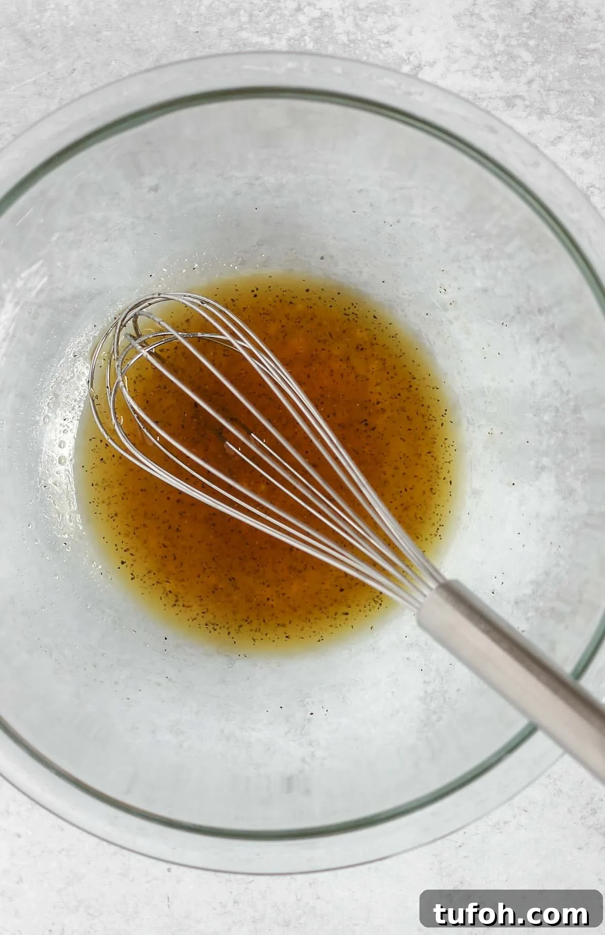 Wire whisk mixing honey marinade in a small glass mixing bowl.