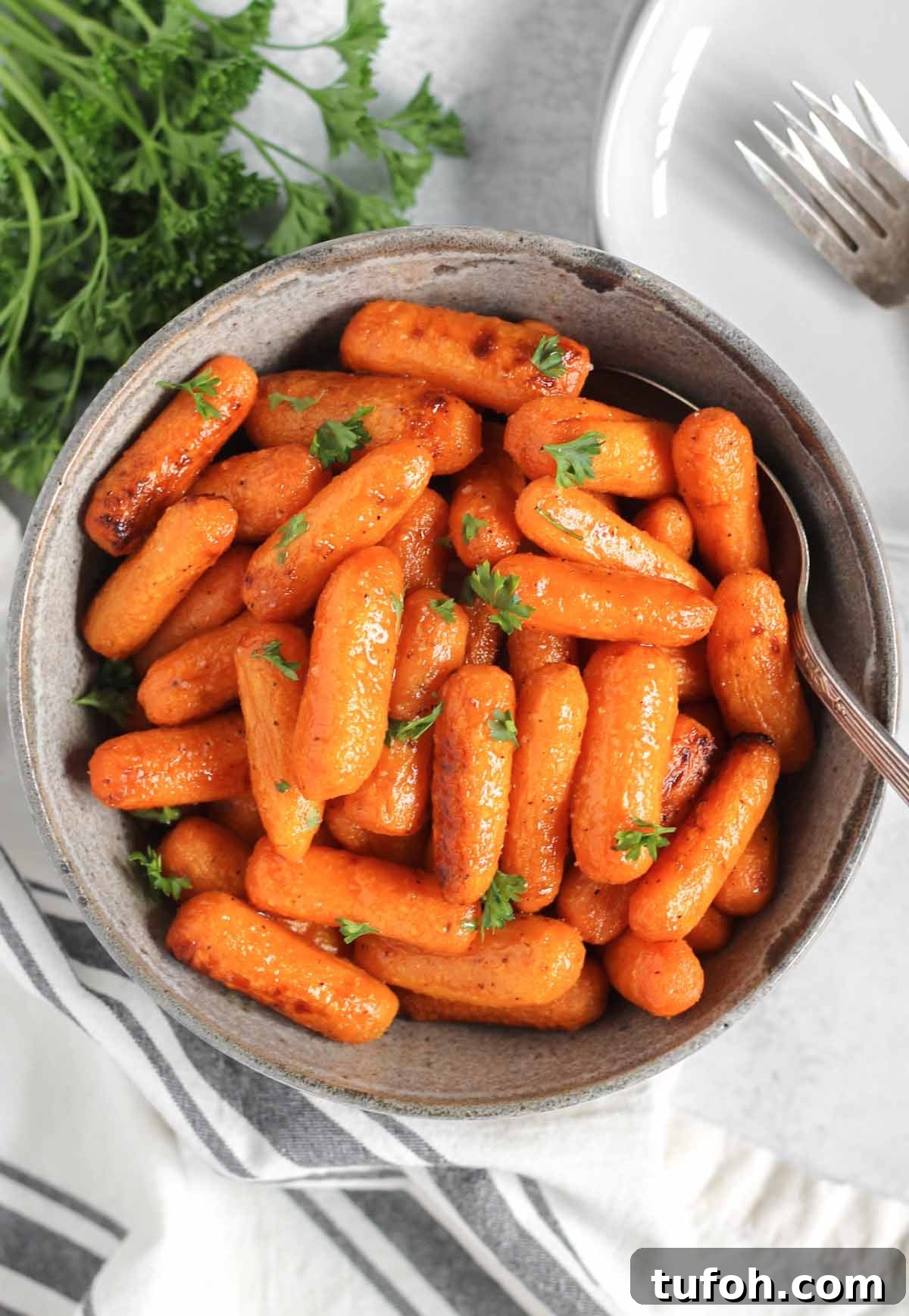 Air fried roasted baby carrots sprinkled with parsley in a gray serving bowl with a spoon.