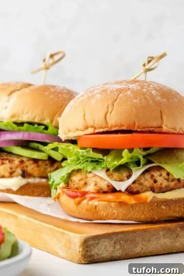 Two air fried turkey burgers with buns on a wood cutting board.