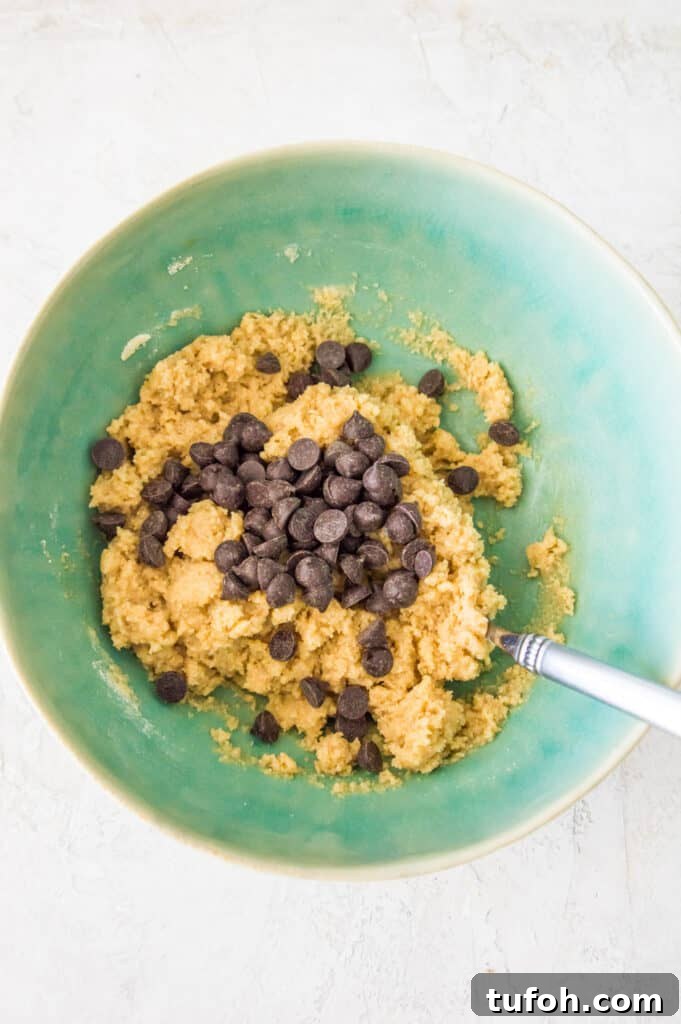 A bowl with raw chocolate chip cookie dough in it with a spoon in it.