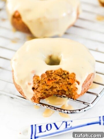 A carrot cake donut with icing on it with a bite out of it.