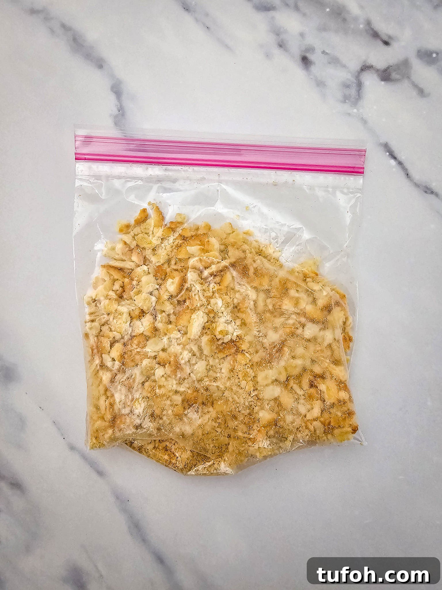 Creamy Cheesy Potato Casserole 7 A plastic bag with crushed crackers, perfect for topping a cheesy potato casserole, sits on a white marble surface.