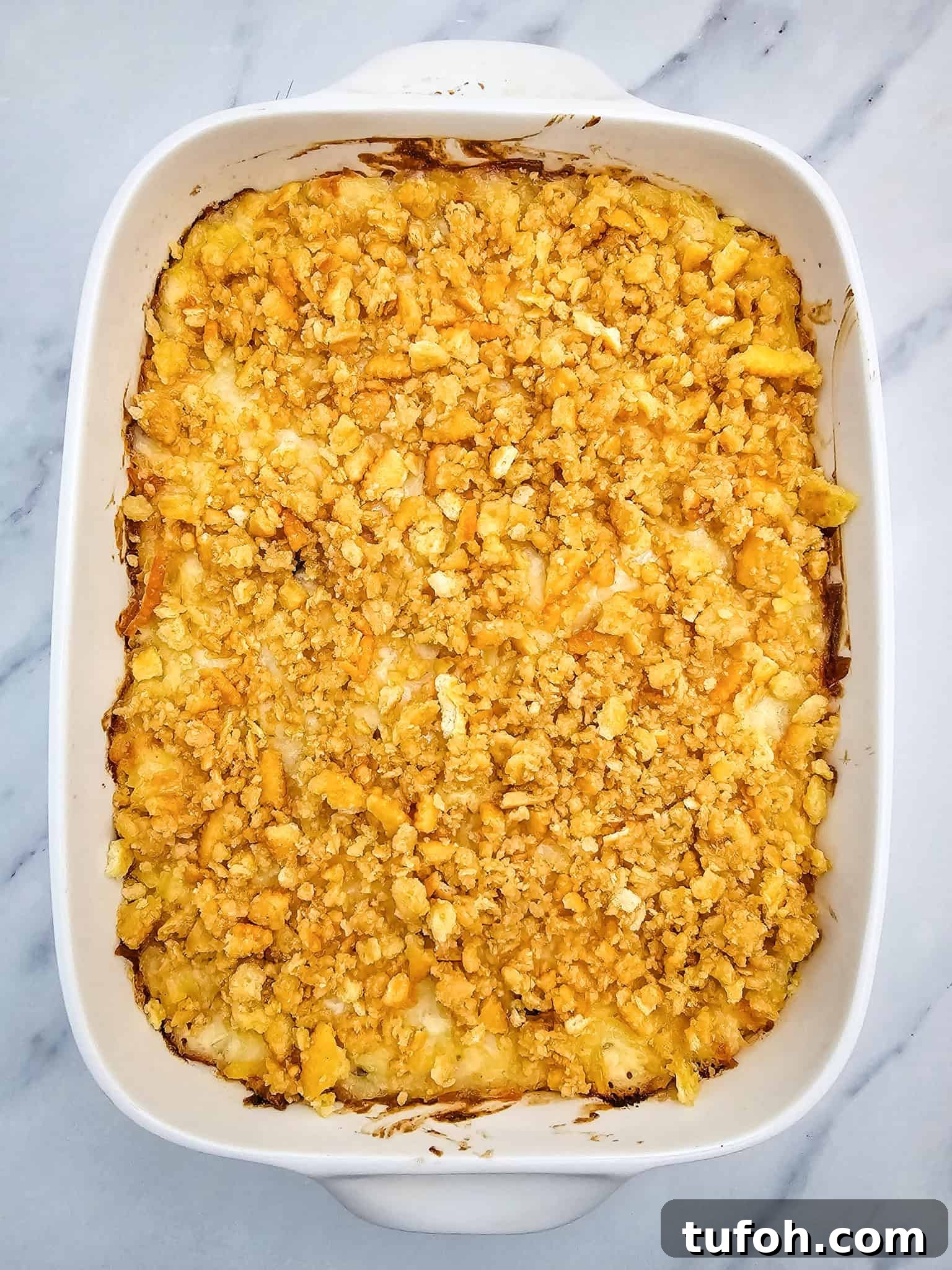 Creamy Cheesy Potato Casserole 8 A white casserole dish filled with a golden, cheesy potato topping rests on a marble surface.