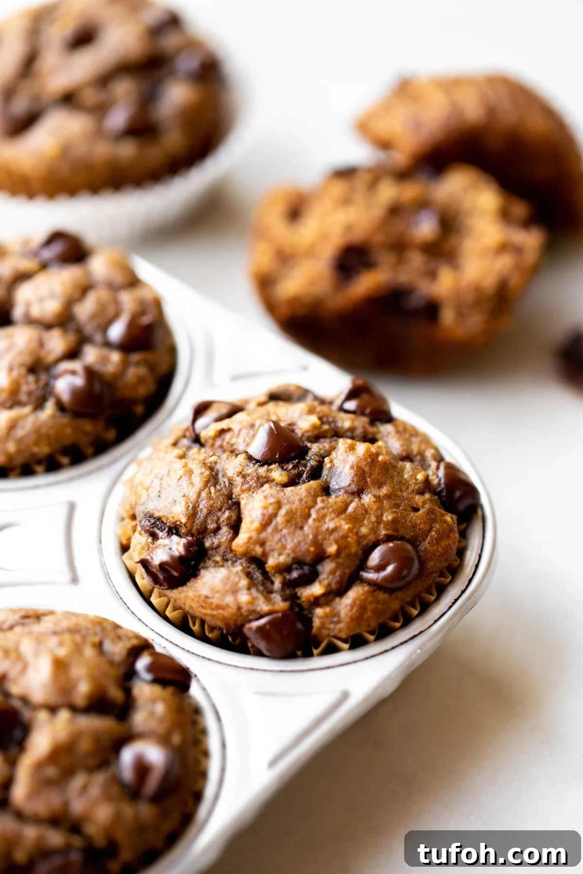 Banana Lentil Muffins: Protein-Packed Breakfast Muffin Recipe 5 closeup photo at 45 degree angle of freshly baked healthy chocolate chip banana muffins in an aluminum muffin pan on a light gray marble background