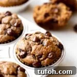 closeup photo at 45 degree angle of freshly baked healthy chocolate chip banana muffins in an aluminum muffin pan on a light gray marble background
