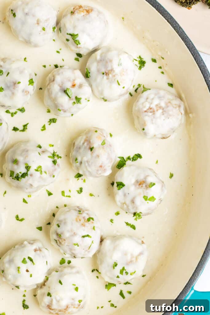 Greek Yogurt Alfredo Meatballs with Creamy Parmesan Sauce 5 Chicken meatballs in alfredo sauce in a pan garnished with finely chopped parsley.