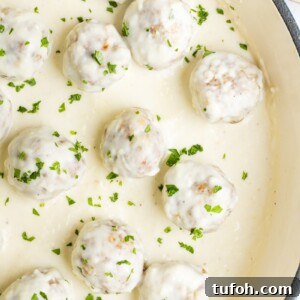 Chicken meatballs in alfredo sauce in a pan garnished with finely chopped parsley.