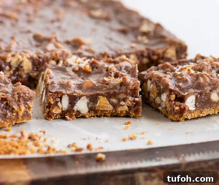 Chewy Nutella Magic Bars: Chocolate-Hazelnut Dessert Squares 2 Nutella magic bars cut into squares on parchment paper showing layers of graham crust, gooey Nutella filling, coconut, baking chips, and chopped nuts.