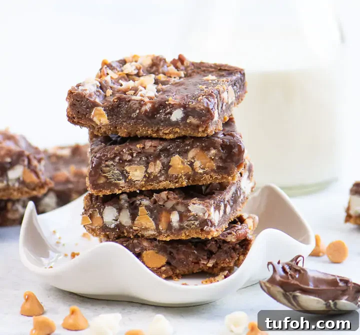 Chewy Nutella Magic Bars: Chocolate-Hazelnut Dessert Squares 5 Stacked Nutella magic bars on a small white dish sliced to show layers of graham cracker crust, Nutella, coconut, baking chips, and chopped nuts.