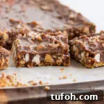 Chewy Nutella Magic Bars: Chocolate-Hazelnut Dessert Squares 6 Nutella magic bars cut into squares on parchment paper showing layers of graham crust, gooey Nutella filling, coconut, baking chips, and chopped nuts.