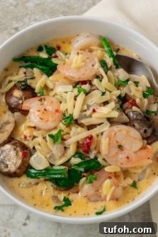 a bowl with a spoon scooing out some shrimp, orzo pasta, mushrooms, spinach, and roasted red peppers in a yellow creamy sauce