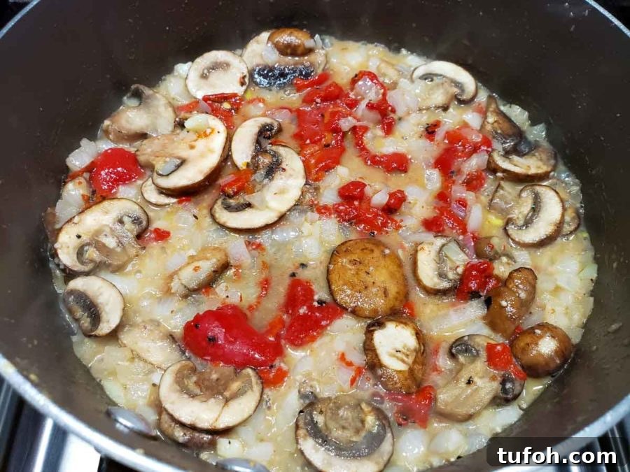 Tuscan Garlic Shrimp with Creamy Orzo 4 a pan filled with mushrooms, roasted red peppers, and onions in a yellow butter sauce
