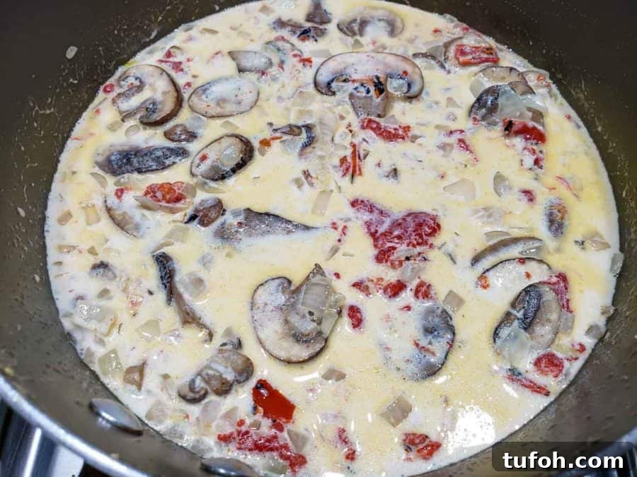 Tuscan Garlic Shrimp with Creamy Orzo 5 a pan filled with mushrooms, roasted red peppers, and onions in a creamy white sauce