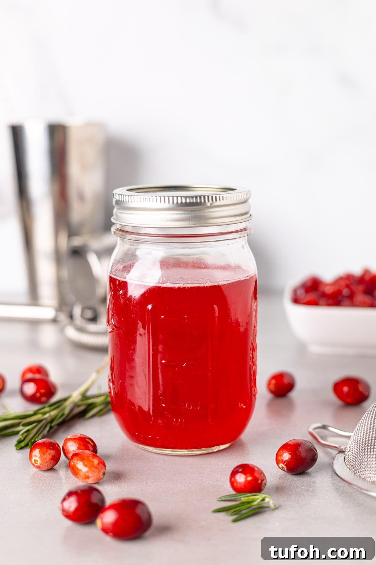 A mason jar with bright red cranberry simple syrup and fresh cranberries spread around the table.