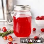 A mason jar with bright red cranberry simple syrup and fresh cranberries spread around the table.