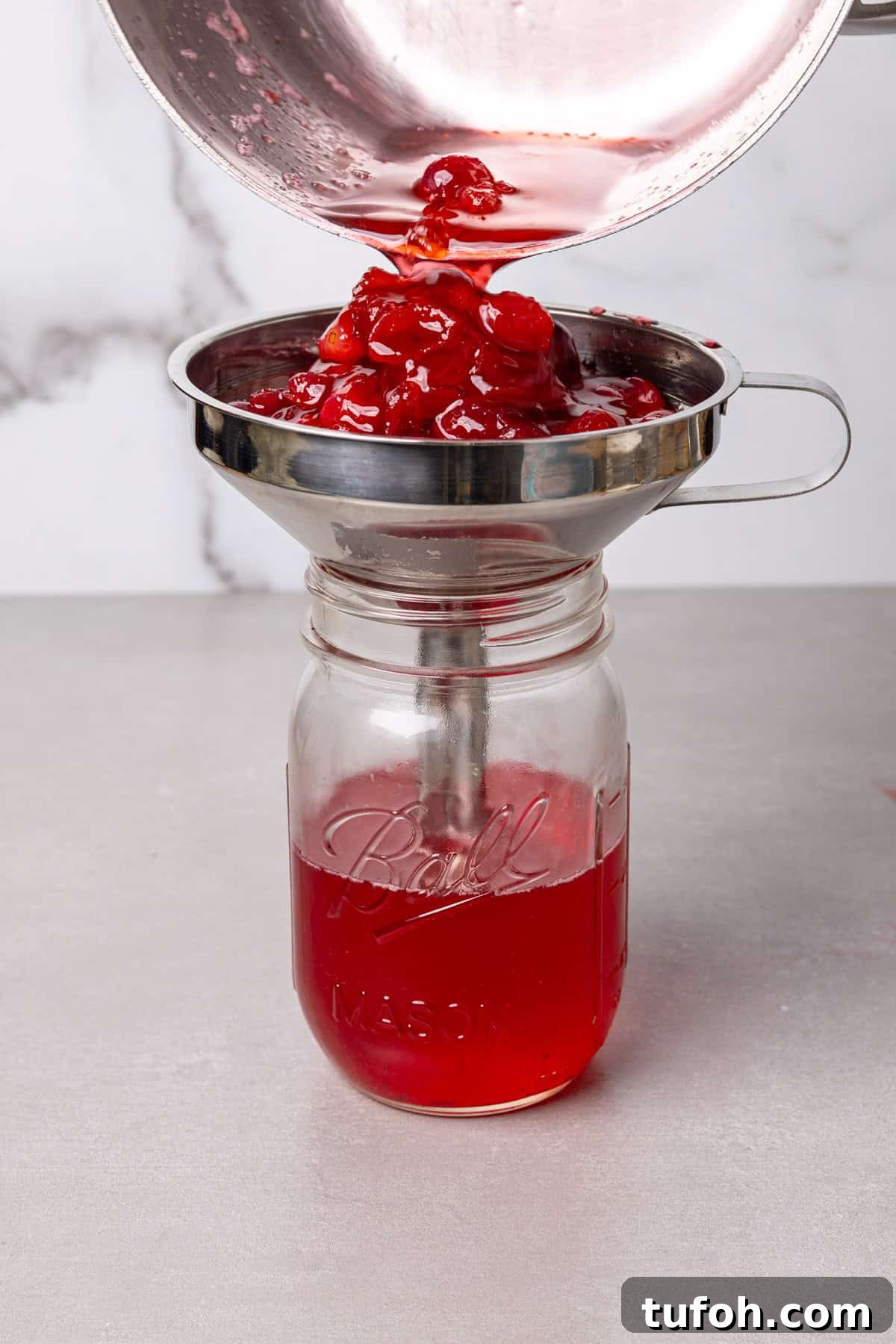 Cranberry simple syrup getting strained into a mason jar.