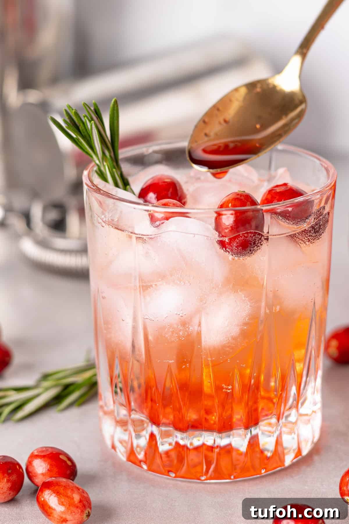 A glass of a cranberry cocktail with a spoon pouring in cranberry simple syrup.