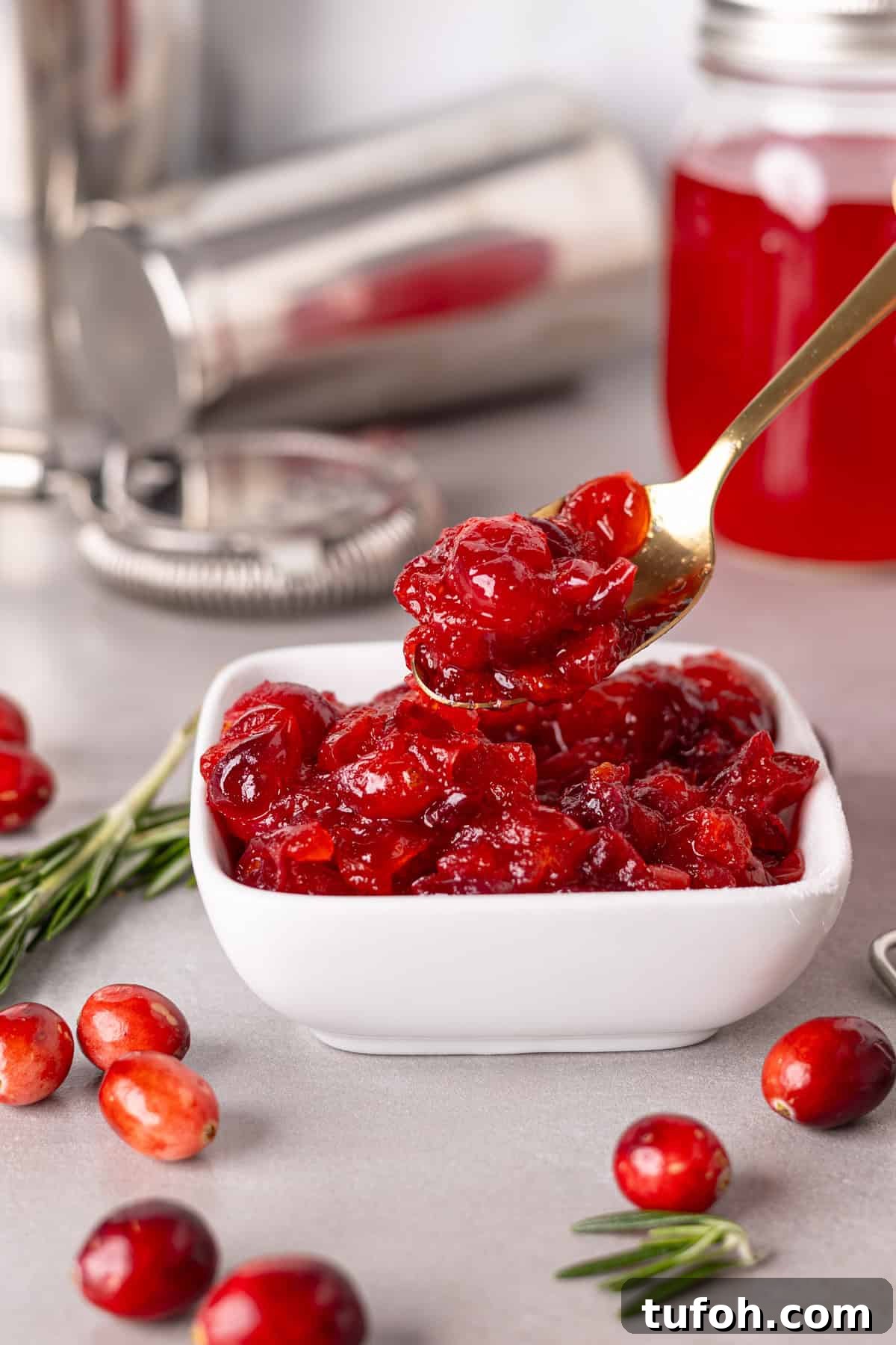 A small white bowl with candies fresh cranberries and a spoon taking out some of the cranberries.