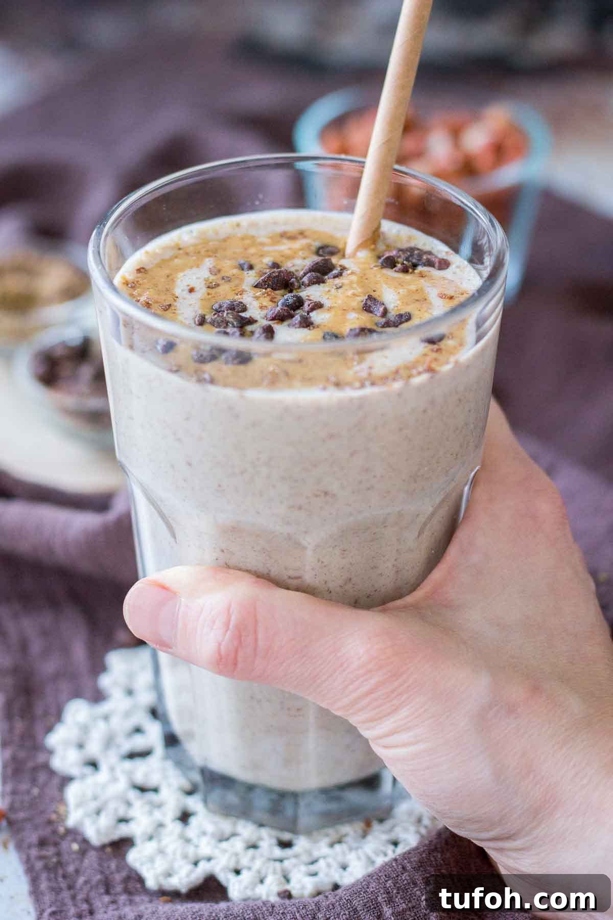 Hand holding a Peanut Butter Protein Shake topped with peanut butter and chocolate served in a glass with a straw