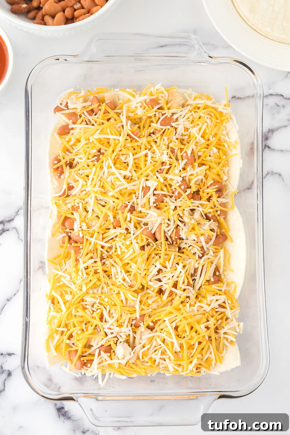 Layered Chicken Enchilada Casserole Recipe — Cheesy Mexican Bake 4 Corn tortillas, chicken cheese, and pinto beans layered in glass baking dish.
