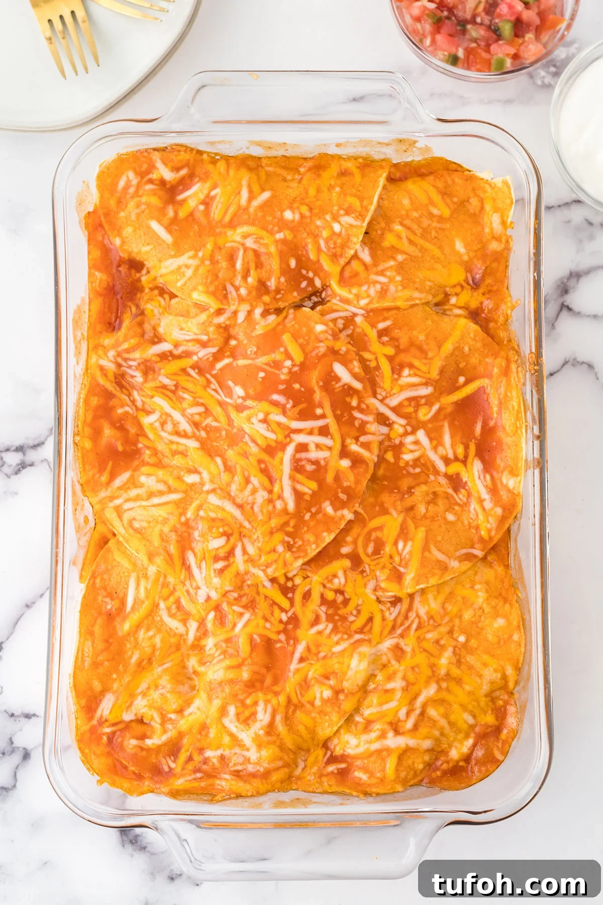 Layered Chicken Enchilada Casserole Recipe — Cheesy Mexican Bake 5 Red sauce poured over chicken enchilada casserole in glass baking dish.