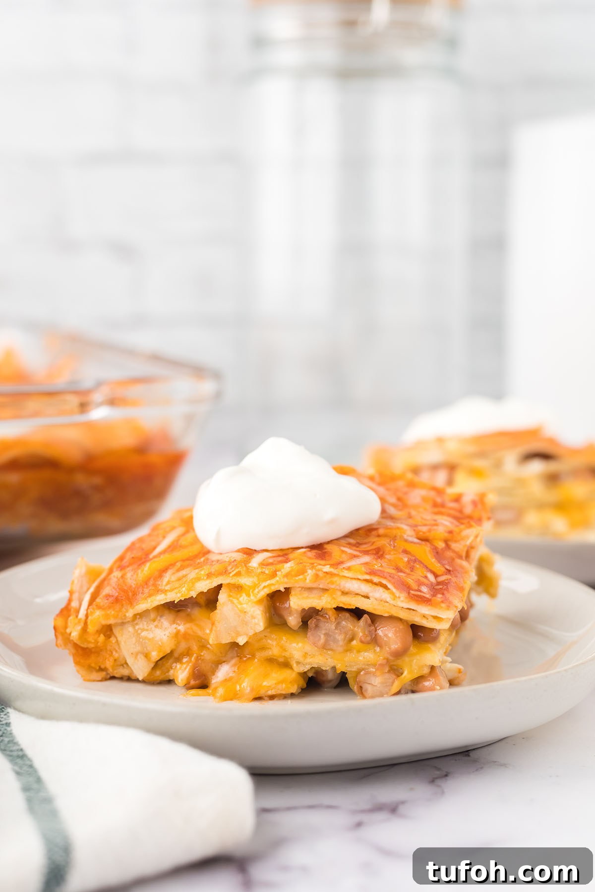 Layered Chicken Enchilada Casserole Recipe — Cheesy Mexican Bake 7 Serving of Chicken Enchilada Casserole topped with sour cream on plate.