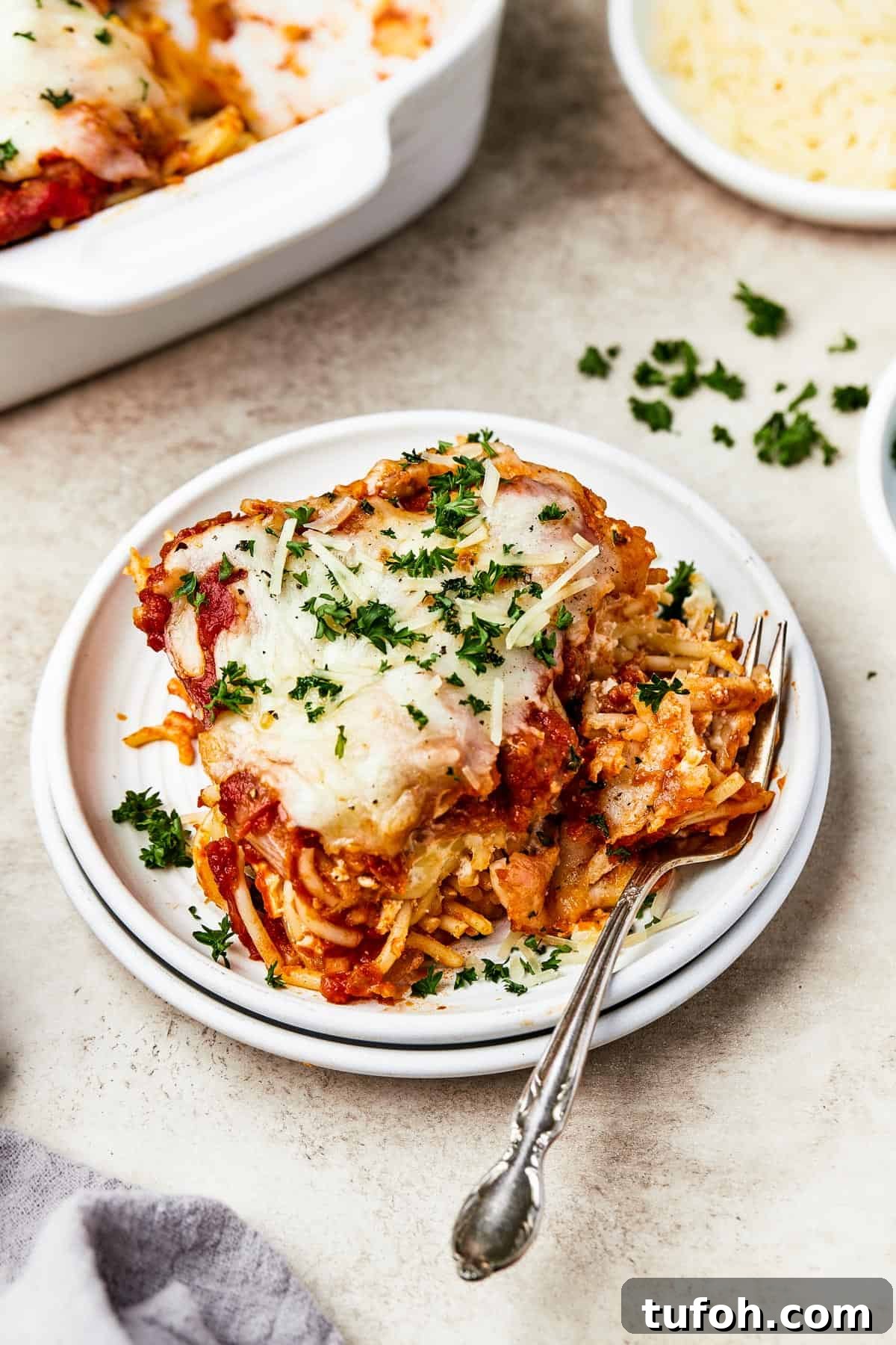 Ultimate Cheesy Baked Spaghetti Casserole Recipe 11 A square of baked spaghetti on a plate, garnished with parsley.
