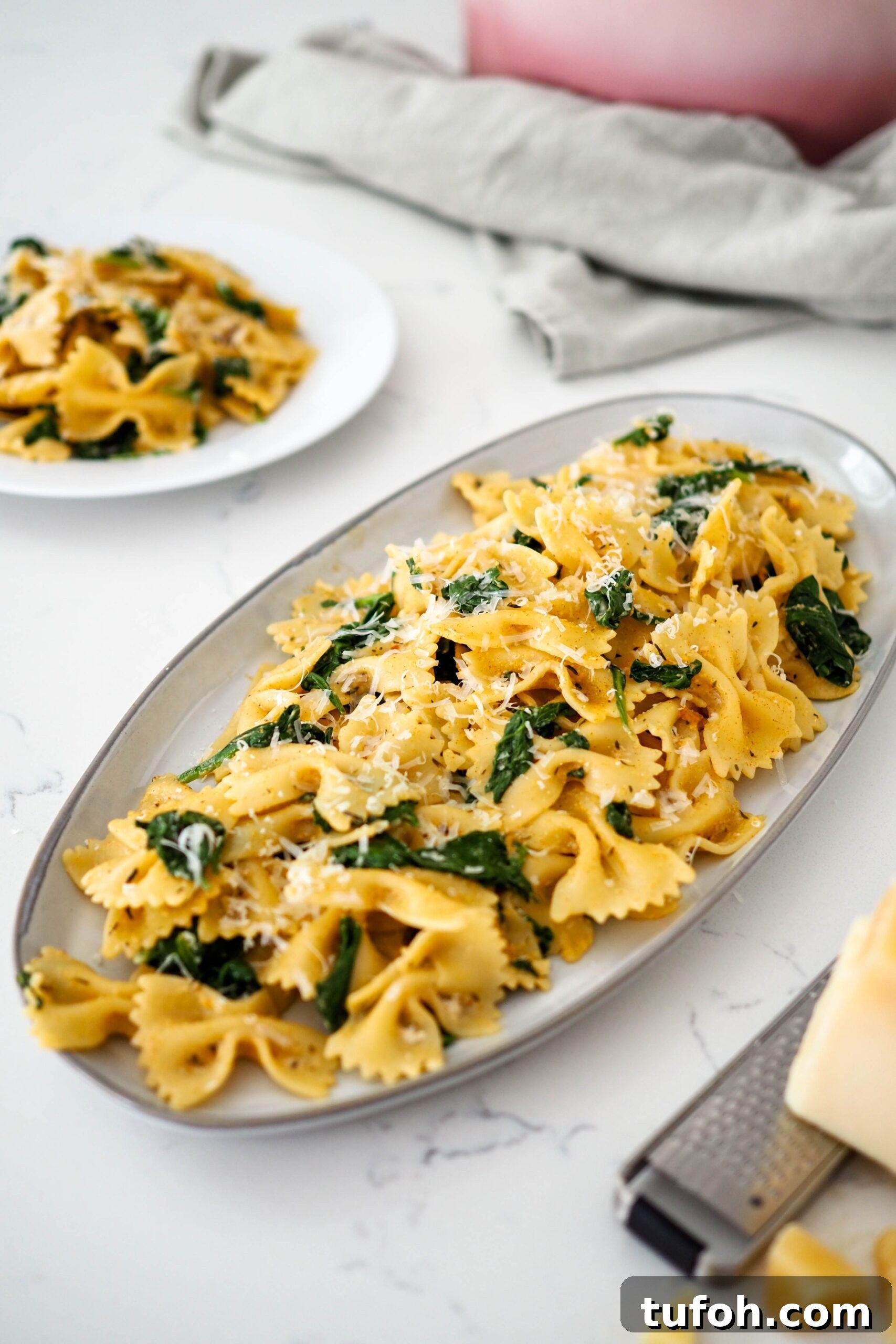 Creamy Cajun Spinach Pasta for Two: Quick Weeknight Recipe 2 A platter of bowtie pasta with wilted spinach and an orangey-red Cajun sauce.