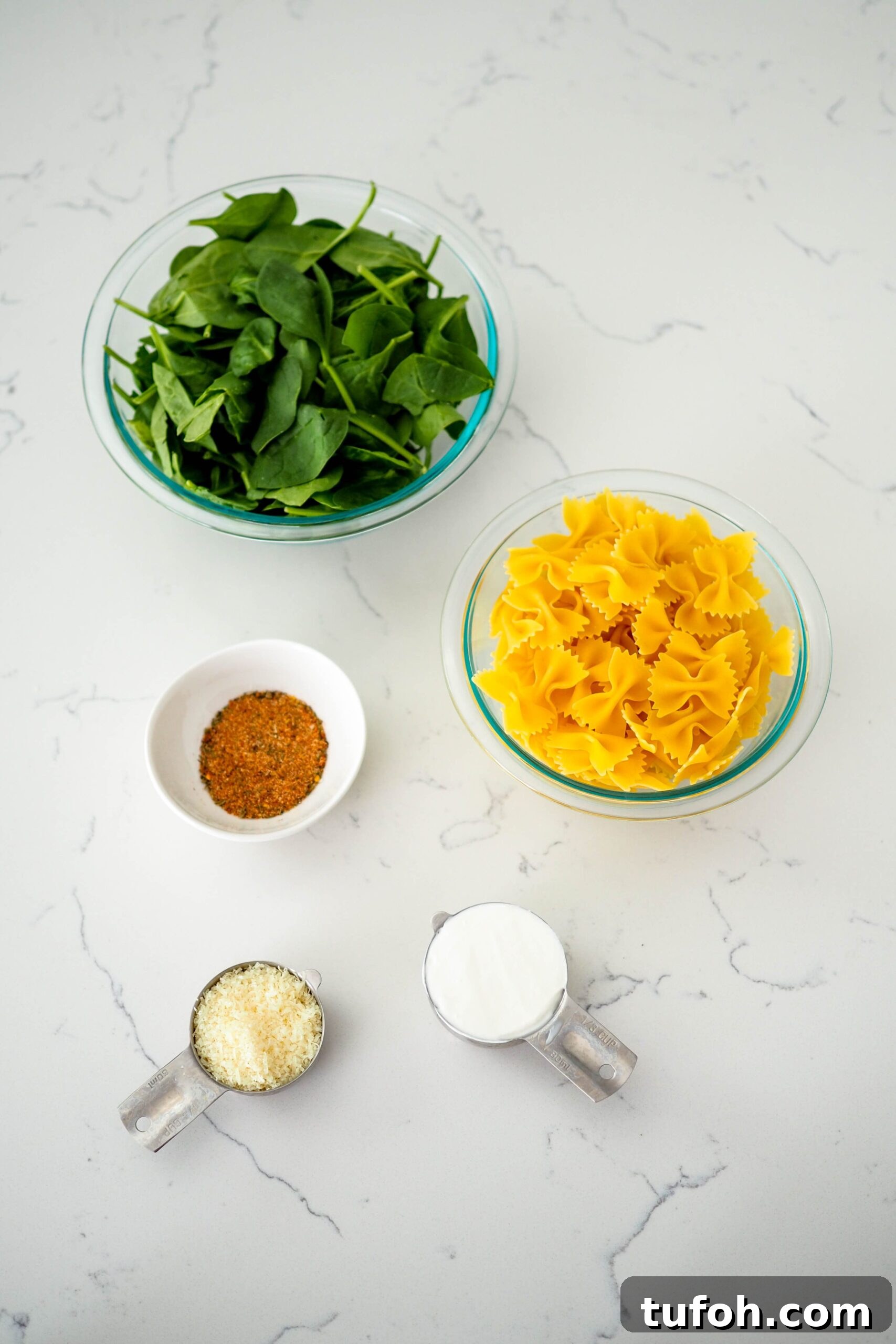 Creamy Cajun Spinach Pasta for Two: Quick Weeknight Recipe 3 Spinach, pasta, sour cream, Parmesan cheese, and Cajun seasoning on a white quartz countertop.