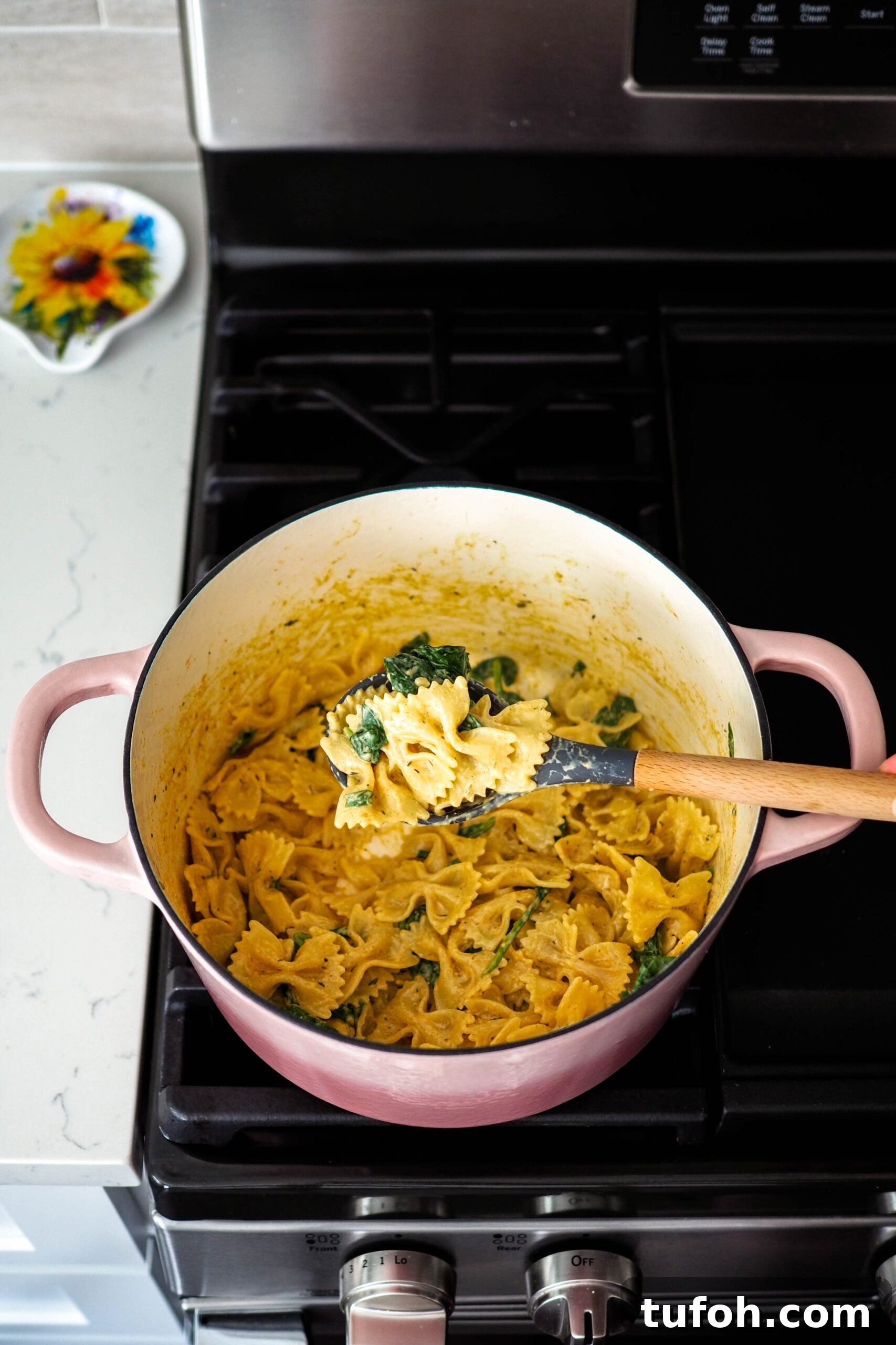 Creamy Cajun Spinach Pasta for Two: Quick Weeknight Recipe 4 A wooden spoon holds up a bite of creamy Cajun spinach pasta out of a Dutch oven on the stove.