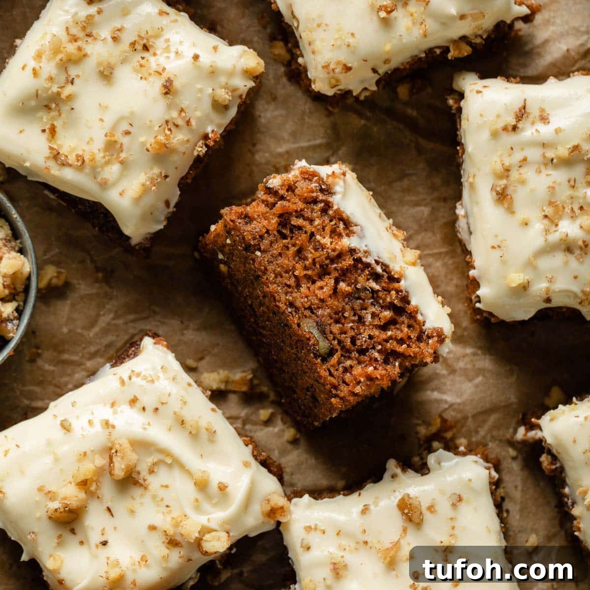 Pieces of carrot cake arranged on parchment paper with a piece turned on its side.