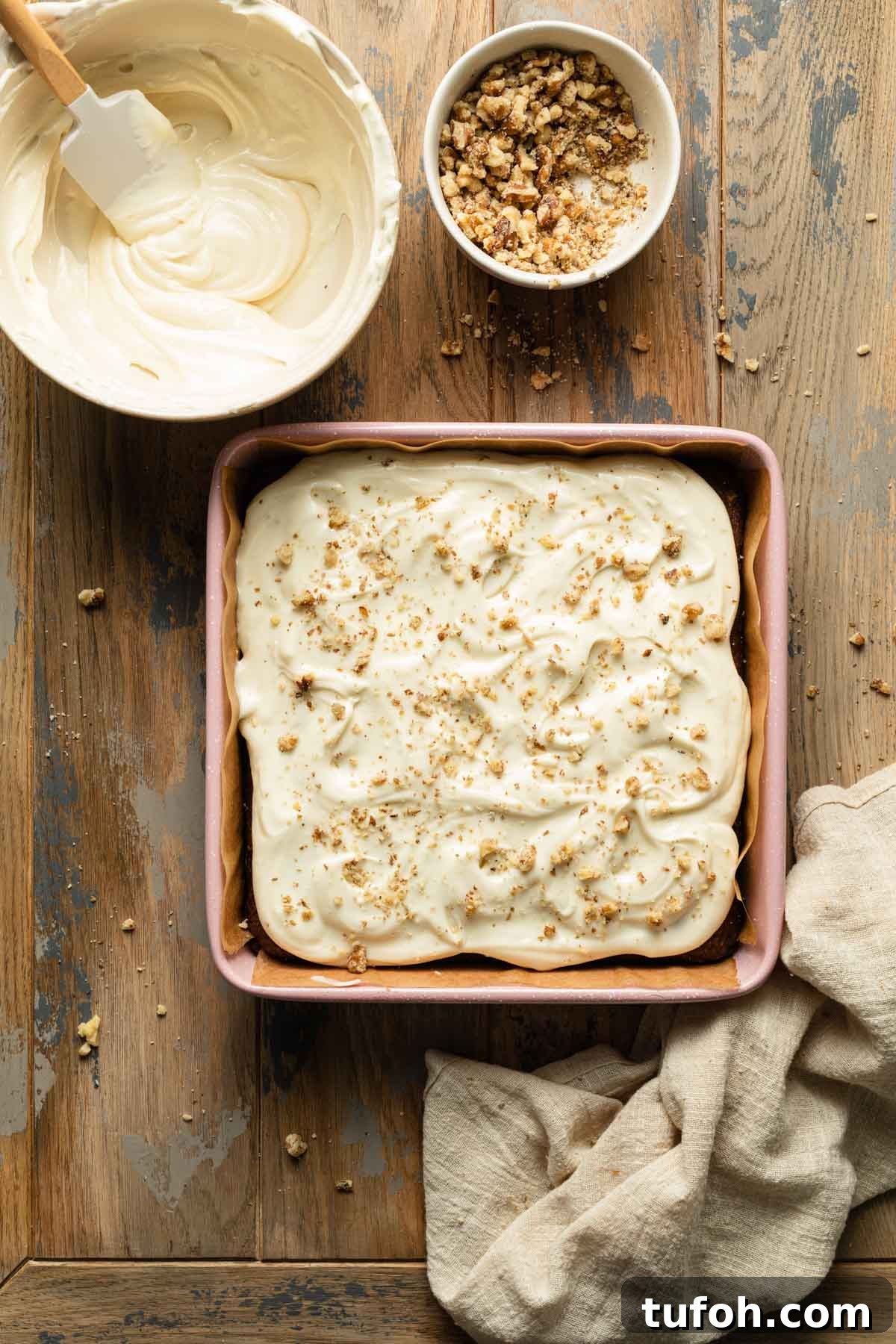 Small carrot cake in a square pan and topped with cream cheese frosting and walnuts.
