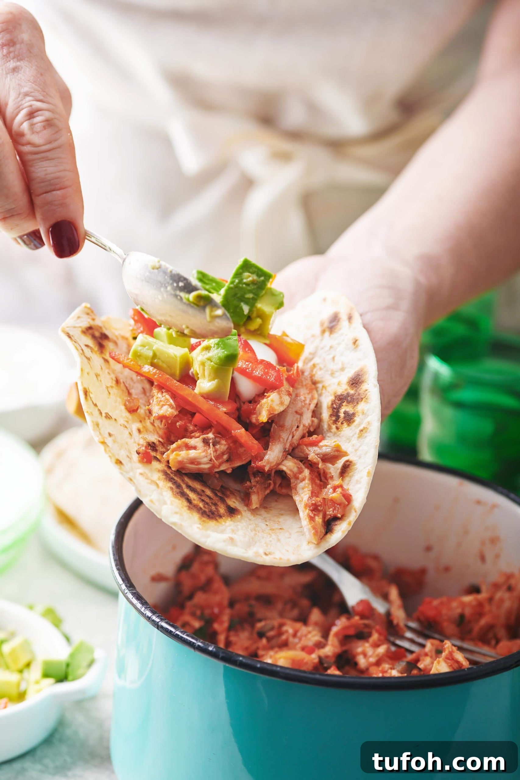 30 Creative Recipes for Leftover Shredded Chicken 3 Spoon scooping avocado onto a Shredded Chicken Taco.