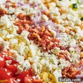 Late Summer Cobb Salad topped with bacon, red onion, crumbled cheese, and other toppings.