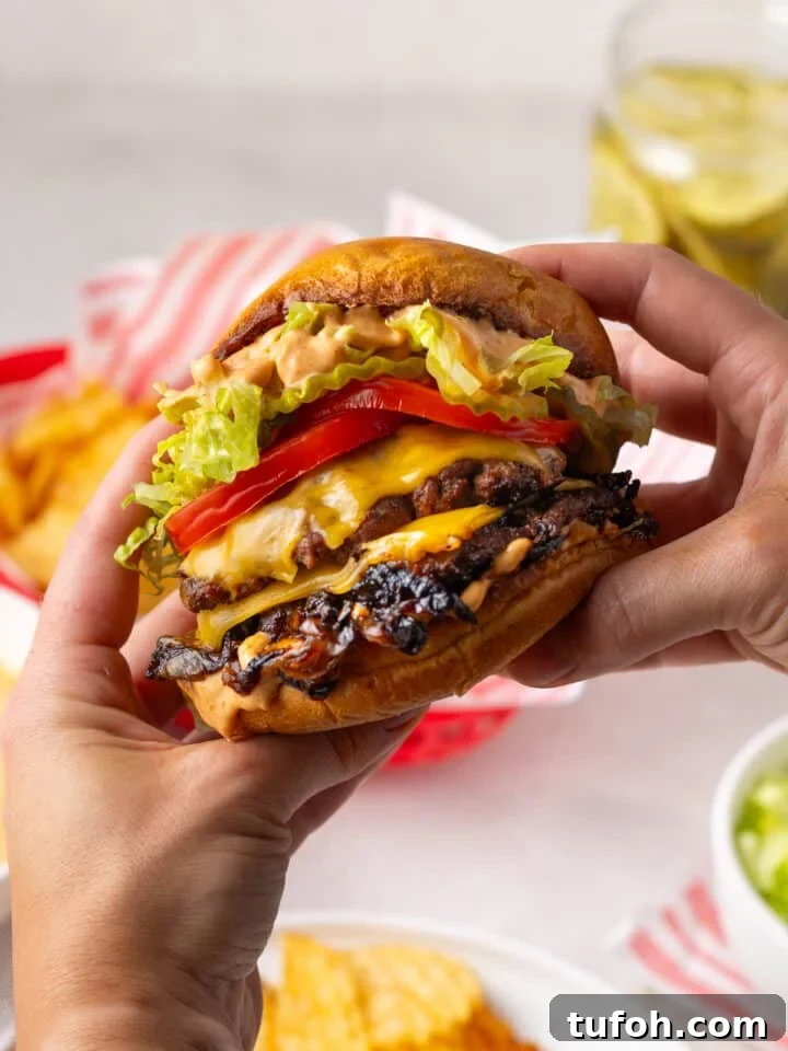 Caramelized Onion Smash Burger — Next-Level Flavor 2 hands holding a smash burger with caramelized onions, tomato, pickles, lettuce and burger sauce