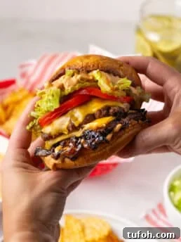 hands holding a caramelized onion smash burger with tomato, pickle, lettuce and special sauce