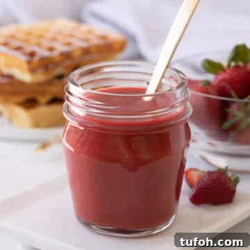Bright red strawberry coulis (strawberry sauce), in a jar with a gold spoon.