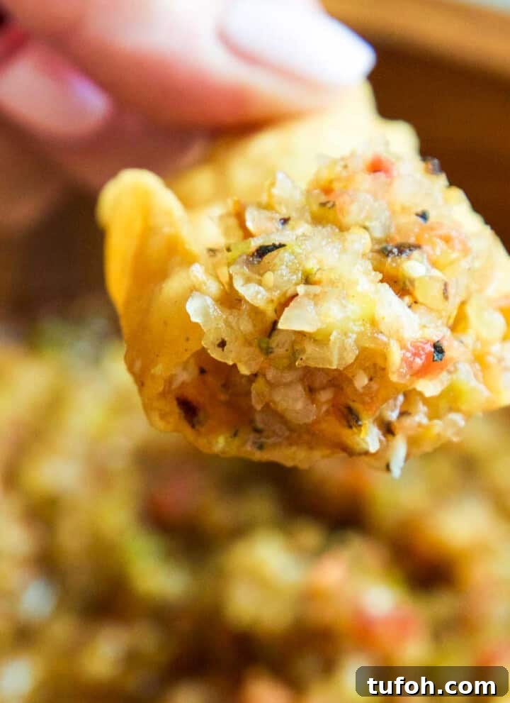 A wood bowl with a lady scooping out homemade salsa with a tortilla chip.