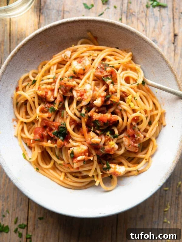 An overhead shot of shrimp spaghetti in a rustic bowl sitting on a wooden surface with a glass of white wine at the side.
