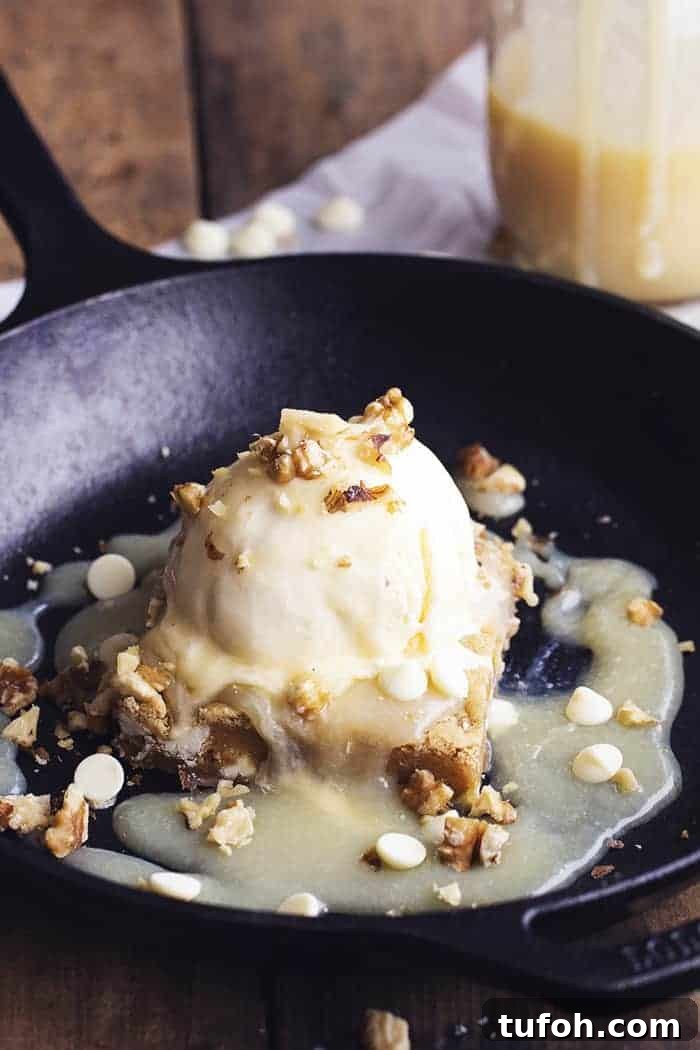 Warm, just-out-of-the-oven white chocolate blondies topped with a scoop of ice cream and drizzled with a silky maple cream sauce—this is one unforgettable dessert! blondies brownie with ice cream in a black skillet.
