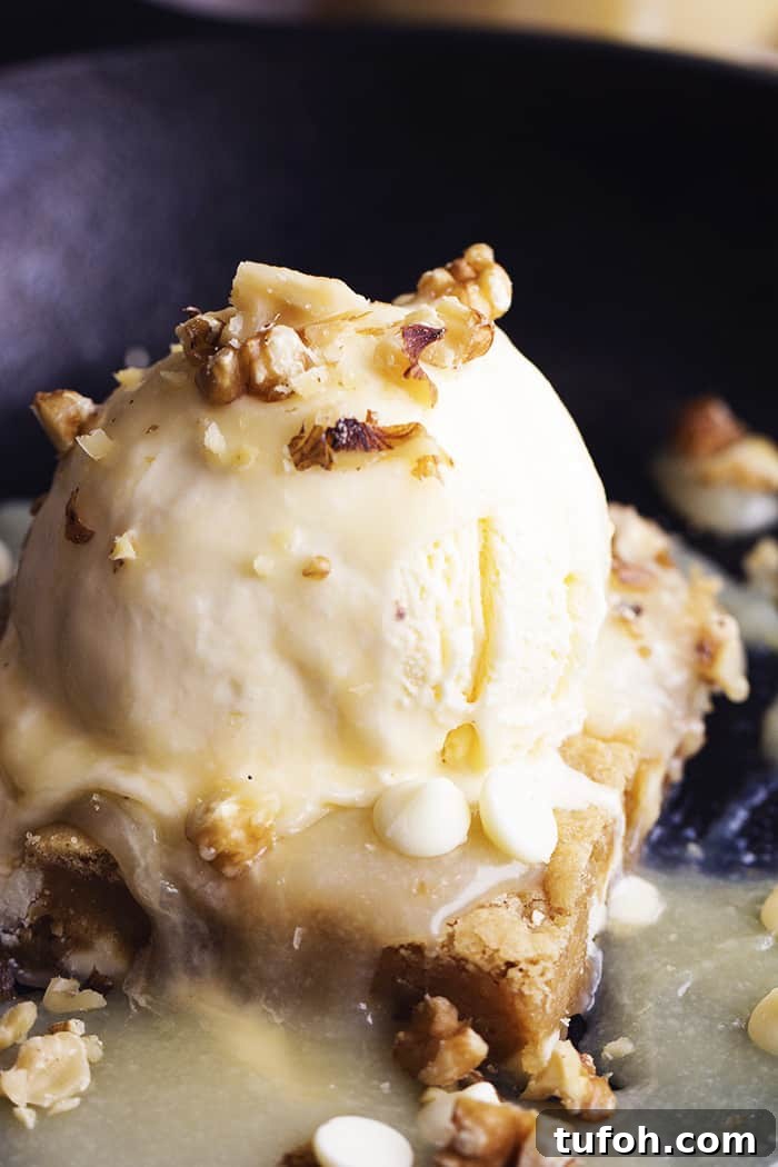 Warm white chocolate blondies with maple cream sauce and ice cream. blondie close up on a black skillet.