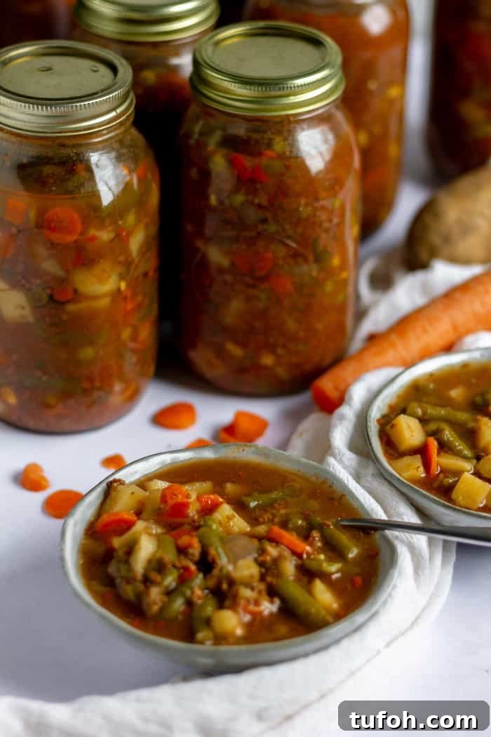 Canning Vegetable Soup at Home: Step-by-Step Guide 3 Image shows several jars of vegetable soup in the background, with two bowls of soup on the counter in front. A spoon rests in one of the bowls.