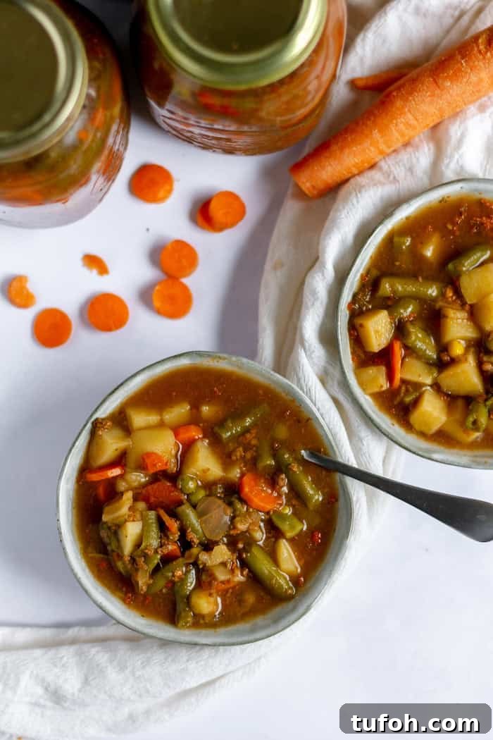 Canning Vegetable Soup at Home: Step-by-Step Guide 4 Image, taken from above, shows two bowls of hearty, vegetable soup, one with a spoon in it. Nearby sit two jars of more soup, and a carrot.