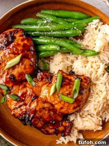 Air fryer teriyaki chicken thighs garnished with sliced green onions and served alongside white rice and green beans.