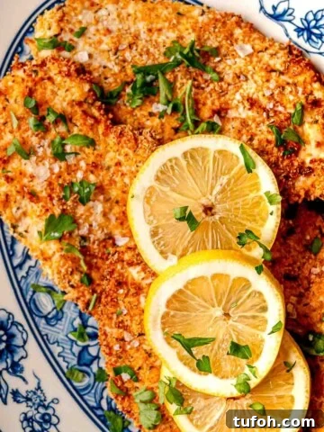 Parmesan-crusted chicken on a blue and white plate, garnished with lemon slices.