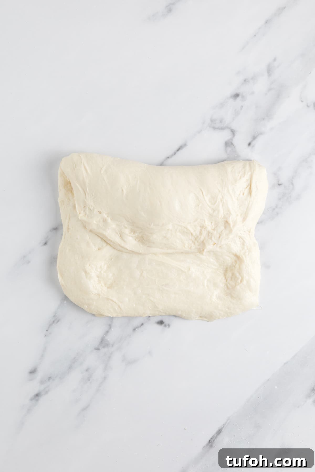 Small-Batch Sourdough Loaf Recipe for Home Bakers 10 Folded small batch sourdough bread dough during the shaping process on a marble countertop.