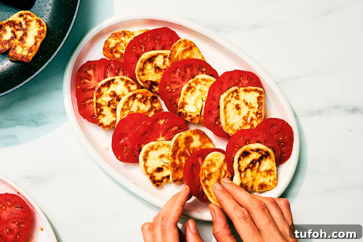 Grilled Halloumi and Tomato Salad with Fresh Herbs 9 Seared halloumi cheese and slices of tomatoes being layered on serving platter.